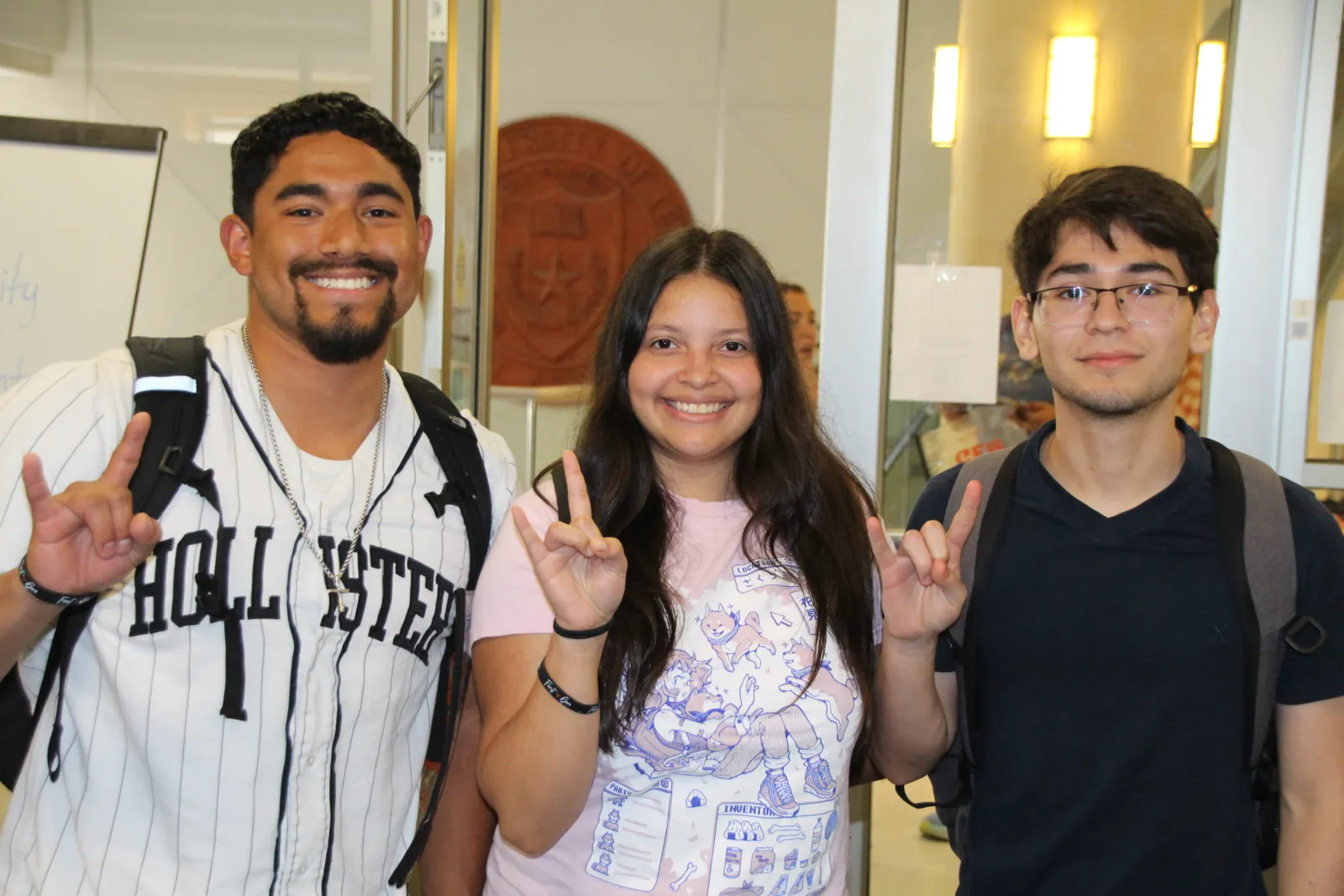 Three first-gen students smiling happily holding up a hook 'em horns symbol at an event.