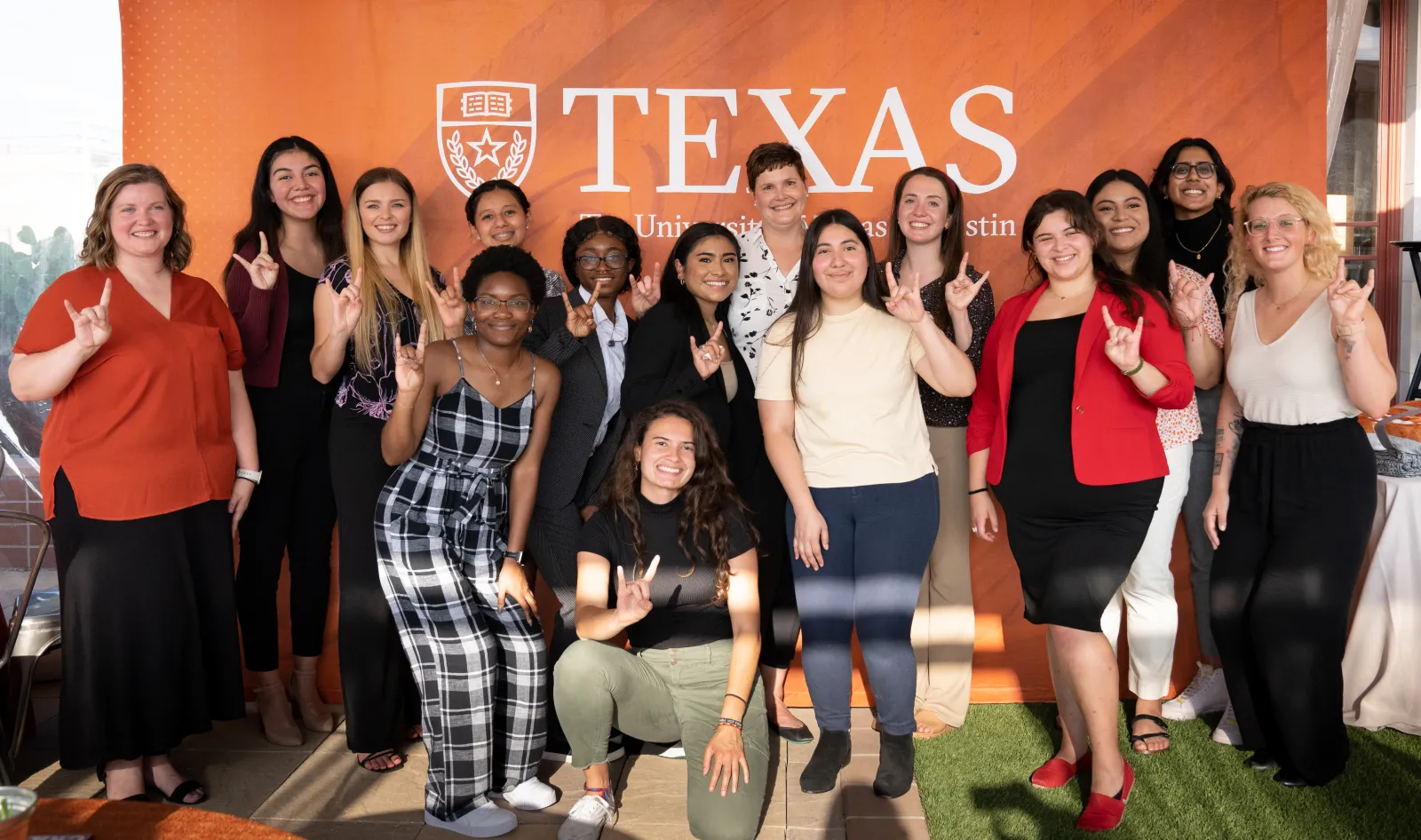 students and staff members standing in front of a burnt orange Texas background