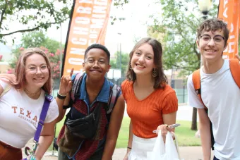 Four smiling university students standing together outdoors near orange banners.