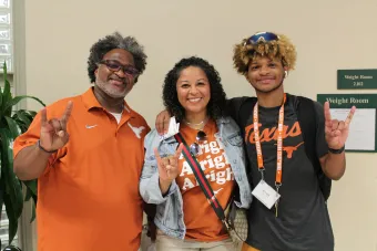 Student posing with guardians with hookem horns hand sign