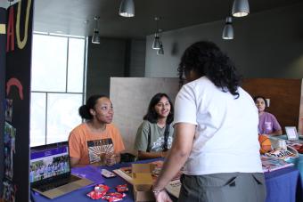 A student talking to two students at a table.
