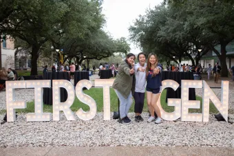Three female students pose with the First-Gen marquee letters.