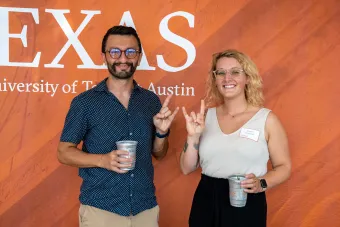 two people standing in front of a burnt orange background holding up the hookem horns handsign