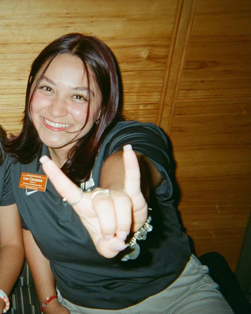 Student holding up a "Hook 'Em" hand sign with a grey shirt and a burnt orange Longhorn Orientation tag