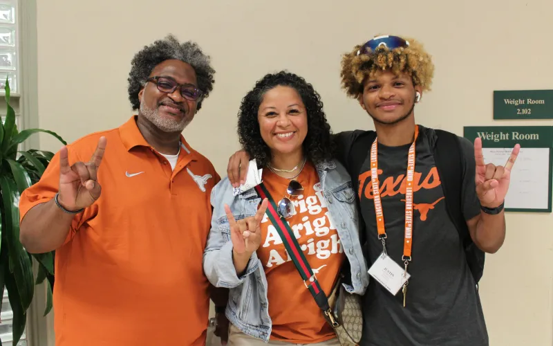 Student posing with guardians with hookem horns hand sign